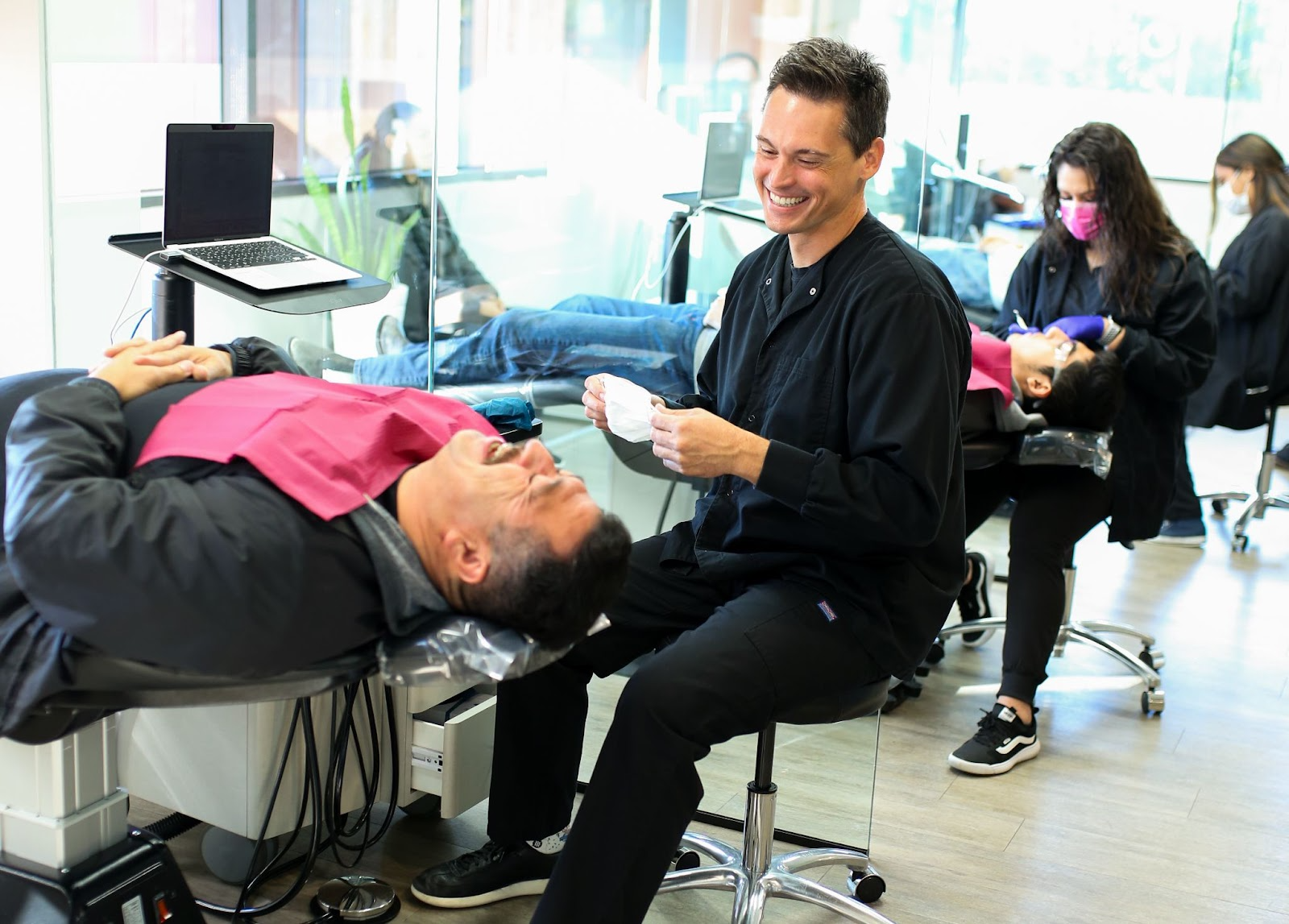 Orthodontist interacting with a patient during a treatment session, showcasing a modern dental office environment with multiple patients receiving care.