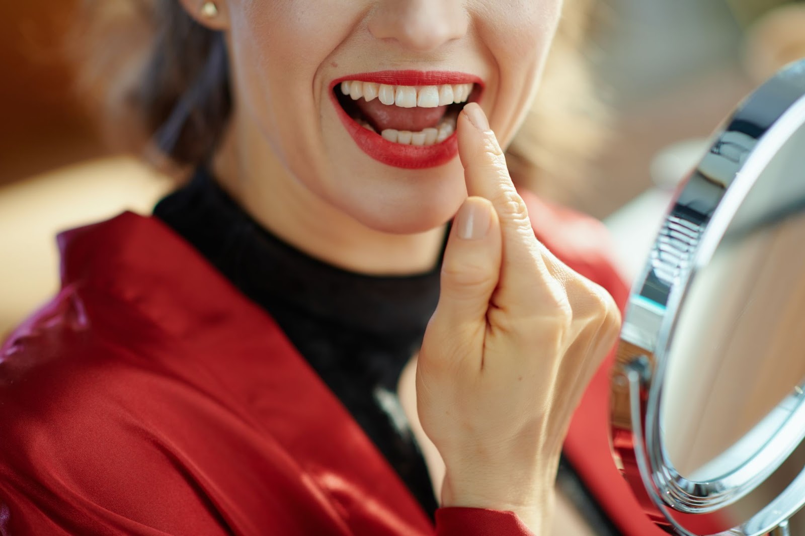 Woman smiling and pointing at her teeth while looking in a mirror, emphasizing post-braces smile care and retainer maintenance.